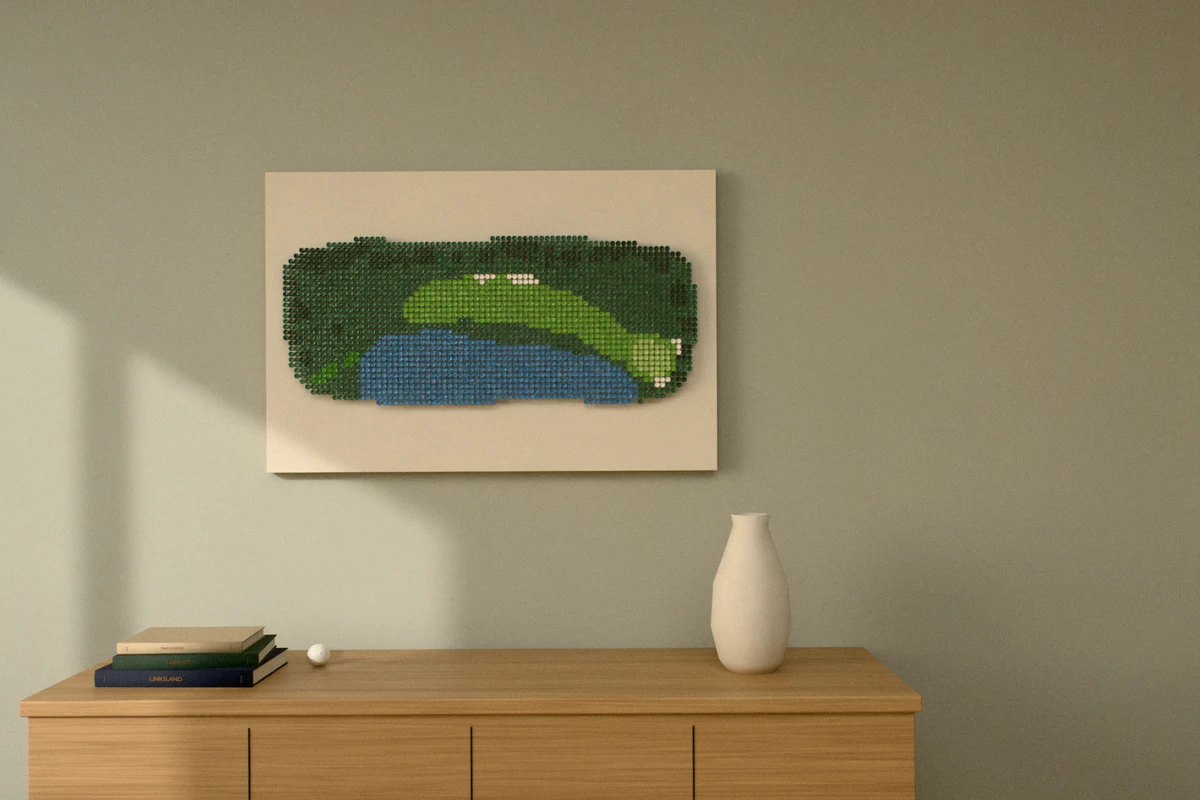 A golf-tee picture of a par 4 that bends around a lake, hung wide on a sage wall above a wooden sideboard with books and a vase.