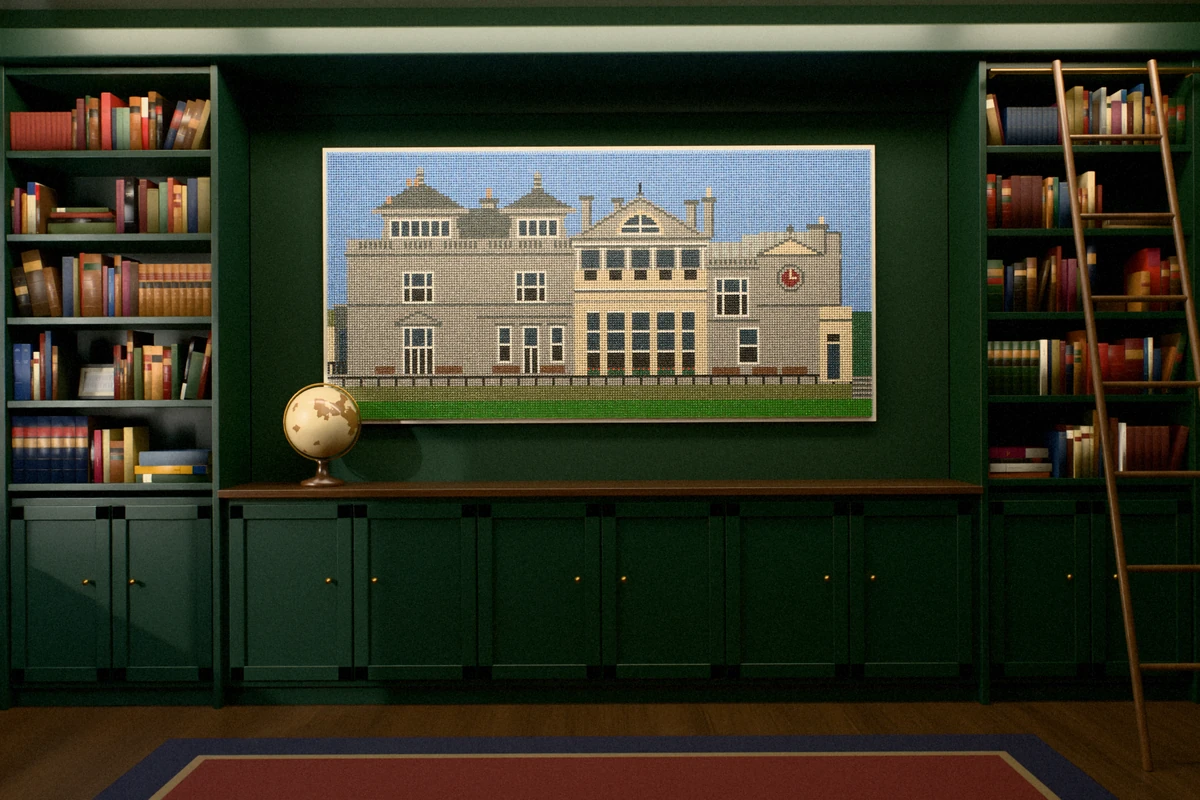 A golf-tee picture of a grand Victorian stone clubhouse with a pillared verandah, a round clock and a clear blue sky, hung over green cupboards between full bookcases in a library.
