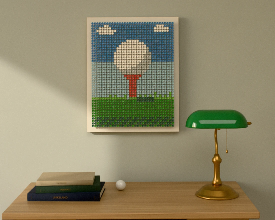 A golf-tee picture of a white ball on a red tee under a blue sky, hung on a sage wall above a small oak writing desk with a green banker’s lamp and books.
